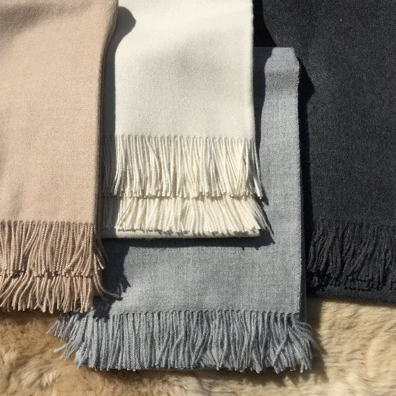 Four alpaca throws in different colors with fringes on a fluffy surface.