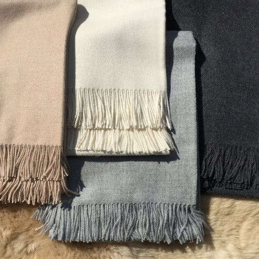 Four alpaca throws in different colors with fringes on a fluffy surface.